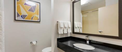A modern bathroom with a black countertop, a white sink, a large mirror, and a toilet.