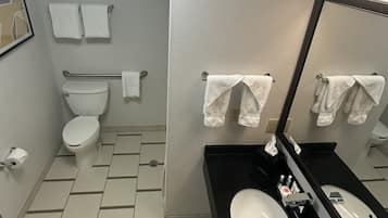 Un baño con inodoro, bidé y lavabo con espejo. Hay toallas colgadas en la pared y un cuadro enmarcado.
