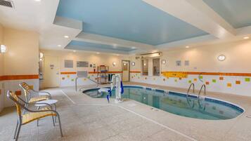 Una piscina interior con suelo de baldosas, una escalera de piscina y dos sillones de descanso.