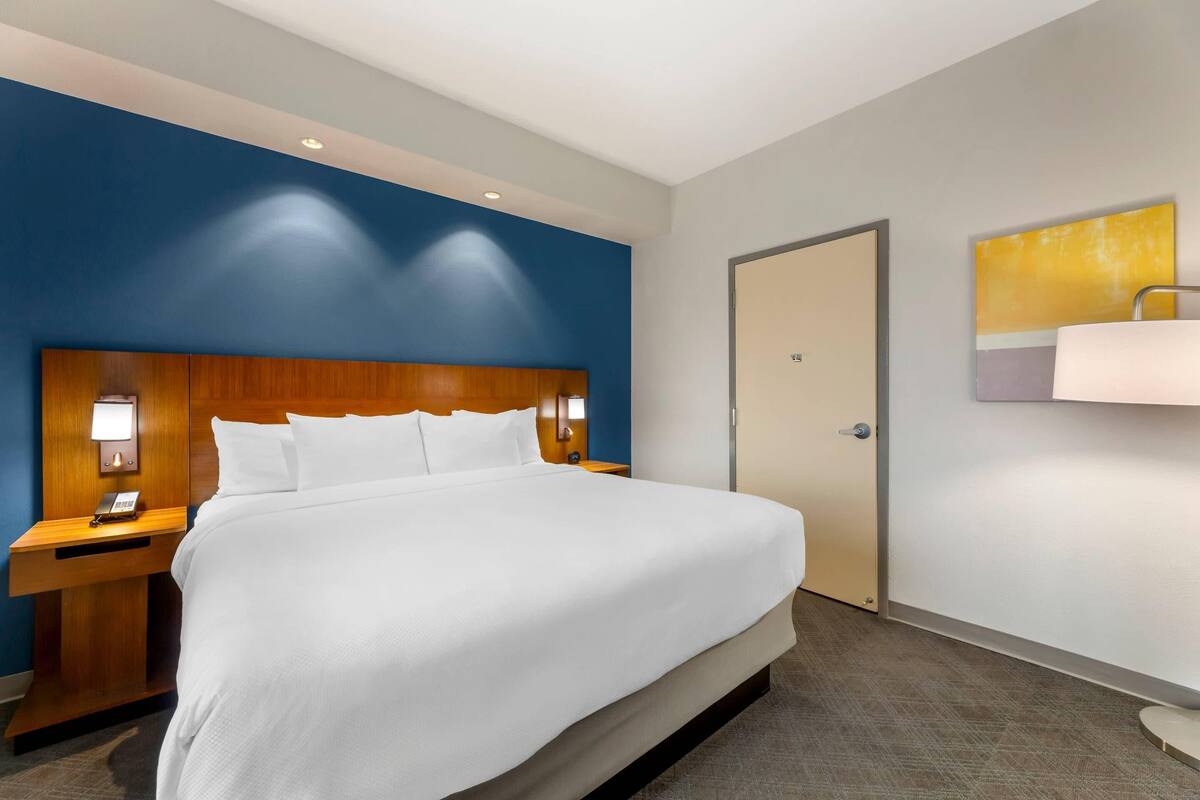 A hotel room with a large bed, wooden headboard, bedside table with a lamp, and a door.