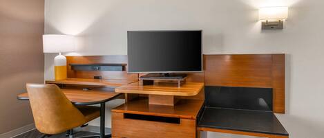 A hotel room with a wooden desk, a television, a chair, and a bedside table.
