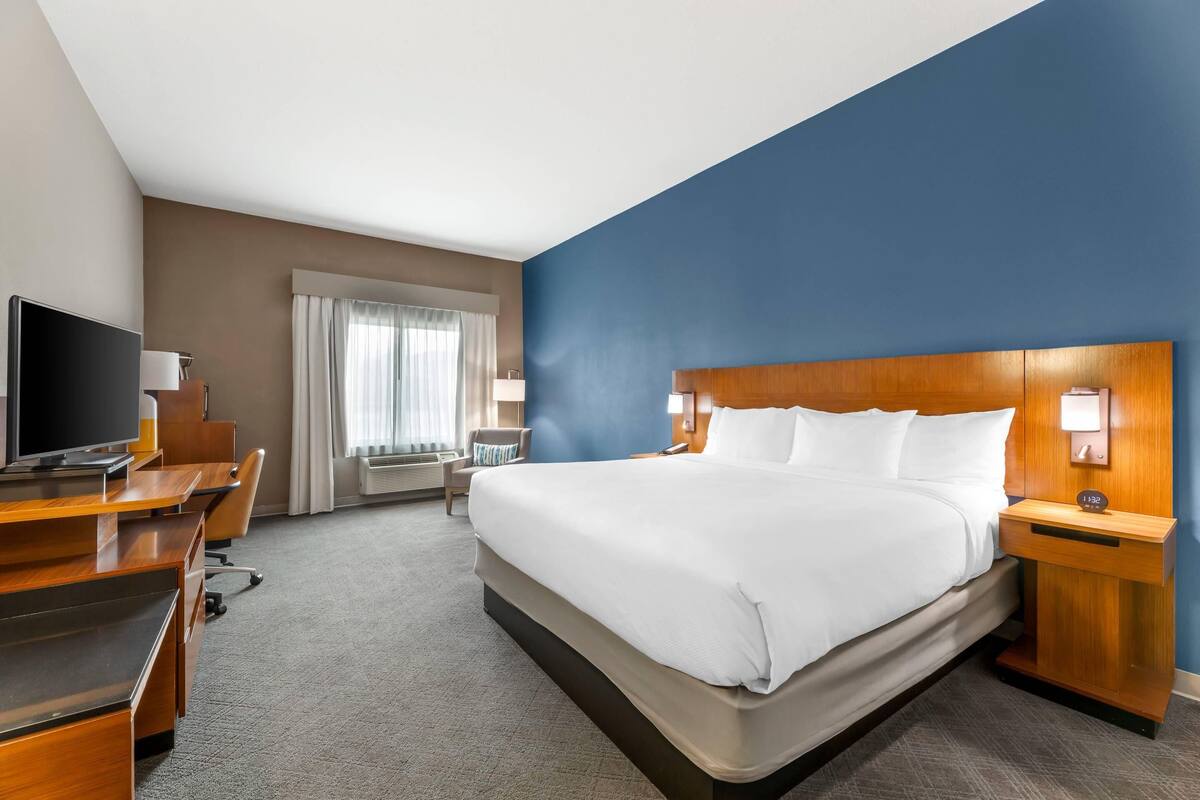 A hotel room with a large bed, a desk with a computer, a television, and a window with curtains.
