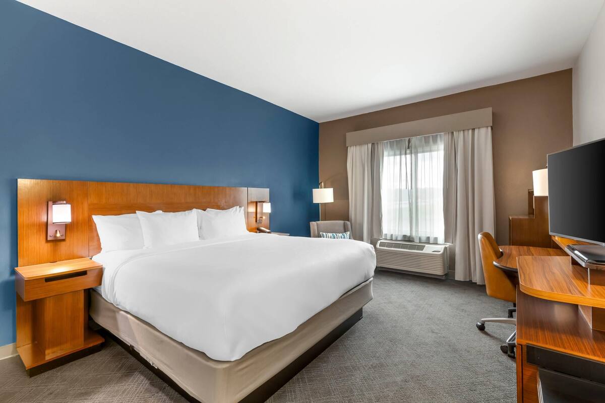 A hotel room with a large bed, a desk, a chair, a TV, and a window with curtains.