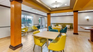 Un comedor espacioso con columnas de madera, sillas amarillas y turquesas, y un amplio ventanal con vistas al exterior.