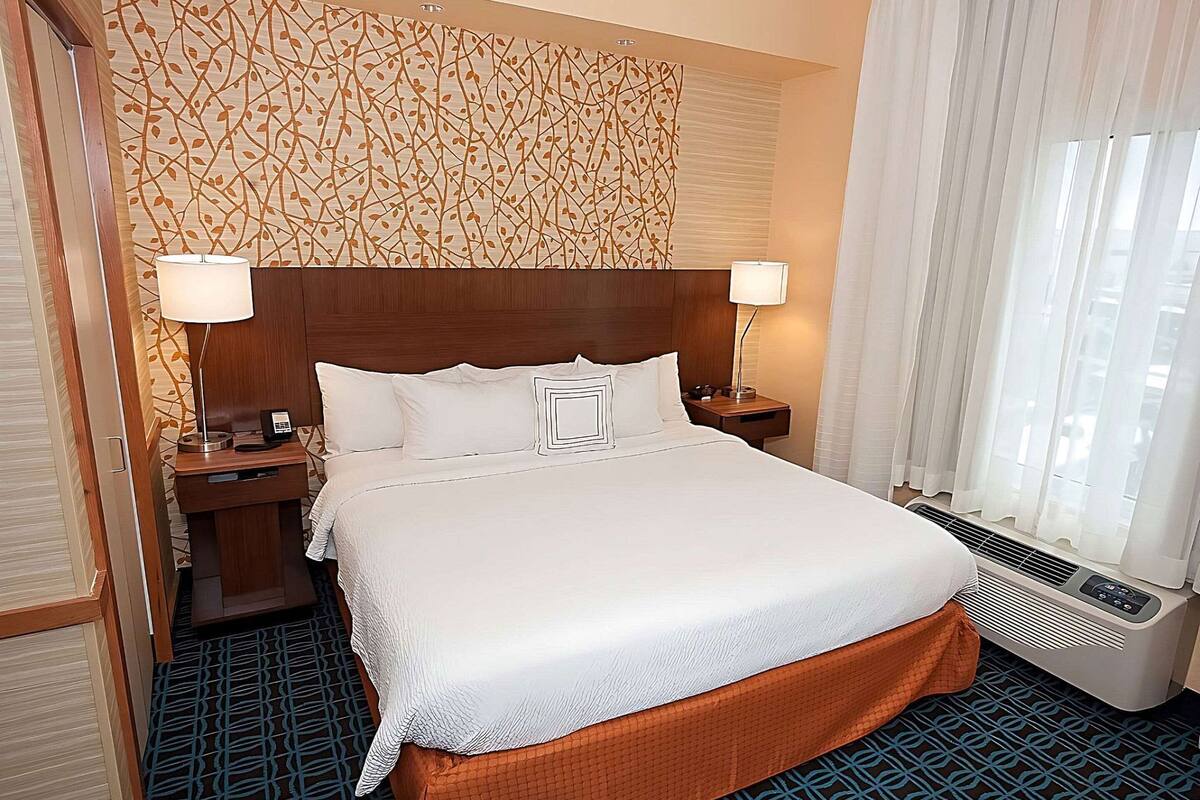 A hotel room with a large bed, two bedside lamps, a telephone, a nightstand, and a window with curtains.