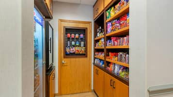 A narrow hallway with a wooden door, shelves stocked with snacks, and a Pepsi refrigerator.