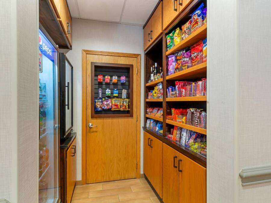 A narrow hallway with a wooden door, shelves stocked with snacks, and a Pepsi refrigerator.