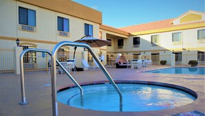 A swimming pool area with metal pool ladders, lounge chairs, and umbrellas. - Oasis Inn & Suites Joshua Tree - 29 Palms (Twentynine Palms)