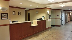 A reception area with a wooden reception desk, a clock, framed pictures on the wall, and a sign with information. - Oasis Inn & Suites Joshua Tree - 29 Palms (Twentynine Palms)
