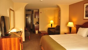 A hotel room with a bed, a desk with a computer, a chair, a lamp, and a television. - Oasis Inn & Suites Joshua Tree - 29 Palms (Twentynine Palms)