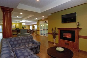A lobby with a fireplace, a television, and a seating area with patterned sofas. - Holiday Inn Express Hotel & Suites Cadillac by IHG (Cadillac)