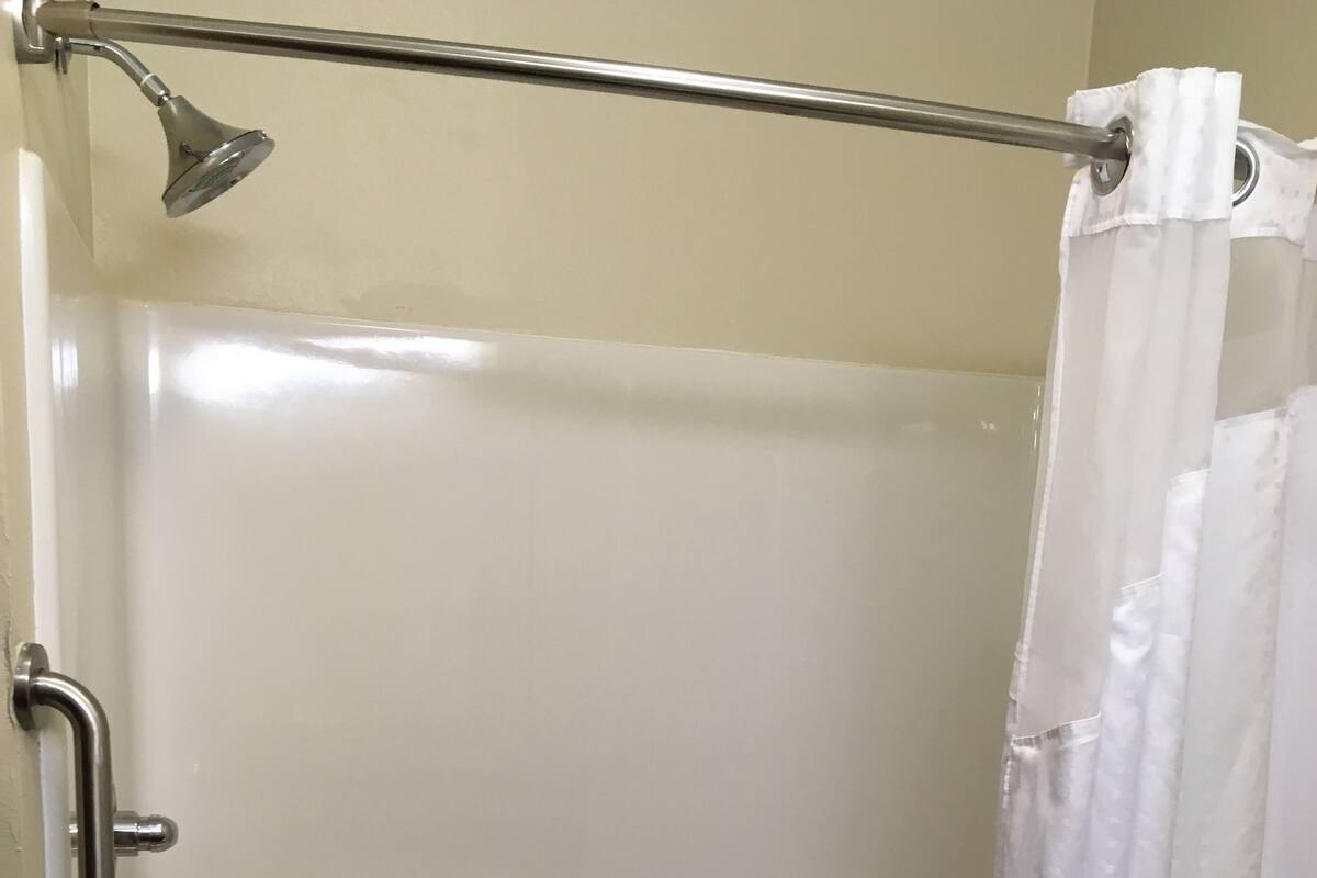 A walk-in shower with a grab bar, a handheld showerhead, and a towel rack.