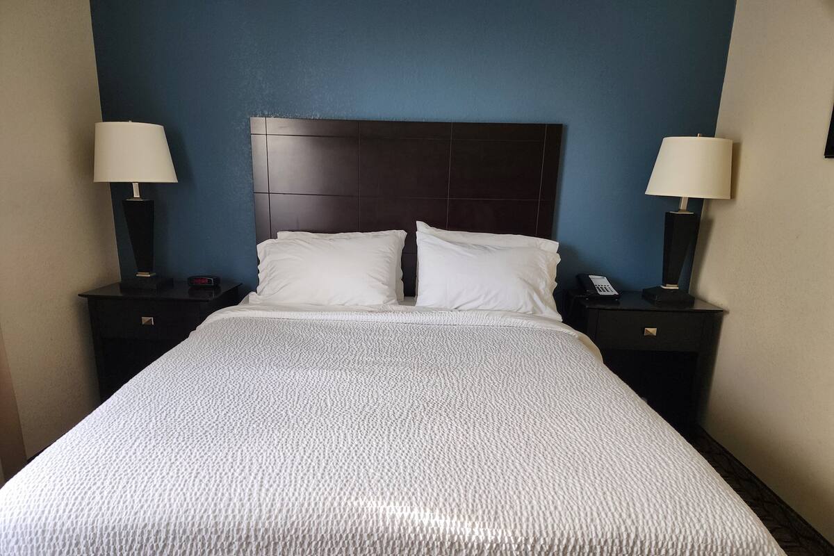 A neatly made bed with white linens, a dark headboard, and two bedside tables with lamps and a phone on each.