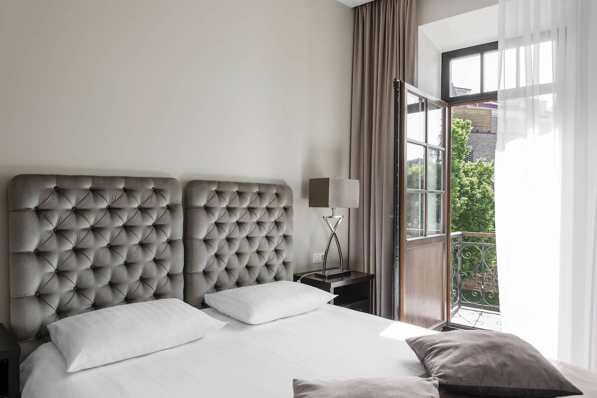 Camera d'albergo con un letto grande, un comodino con una lampada e vista sull'esterno attraverso una finestra.
