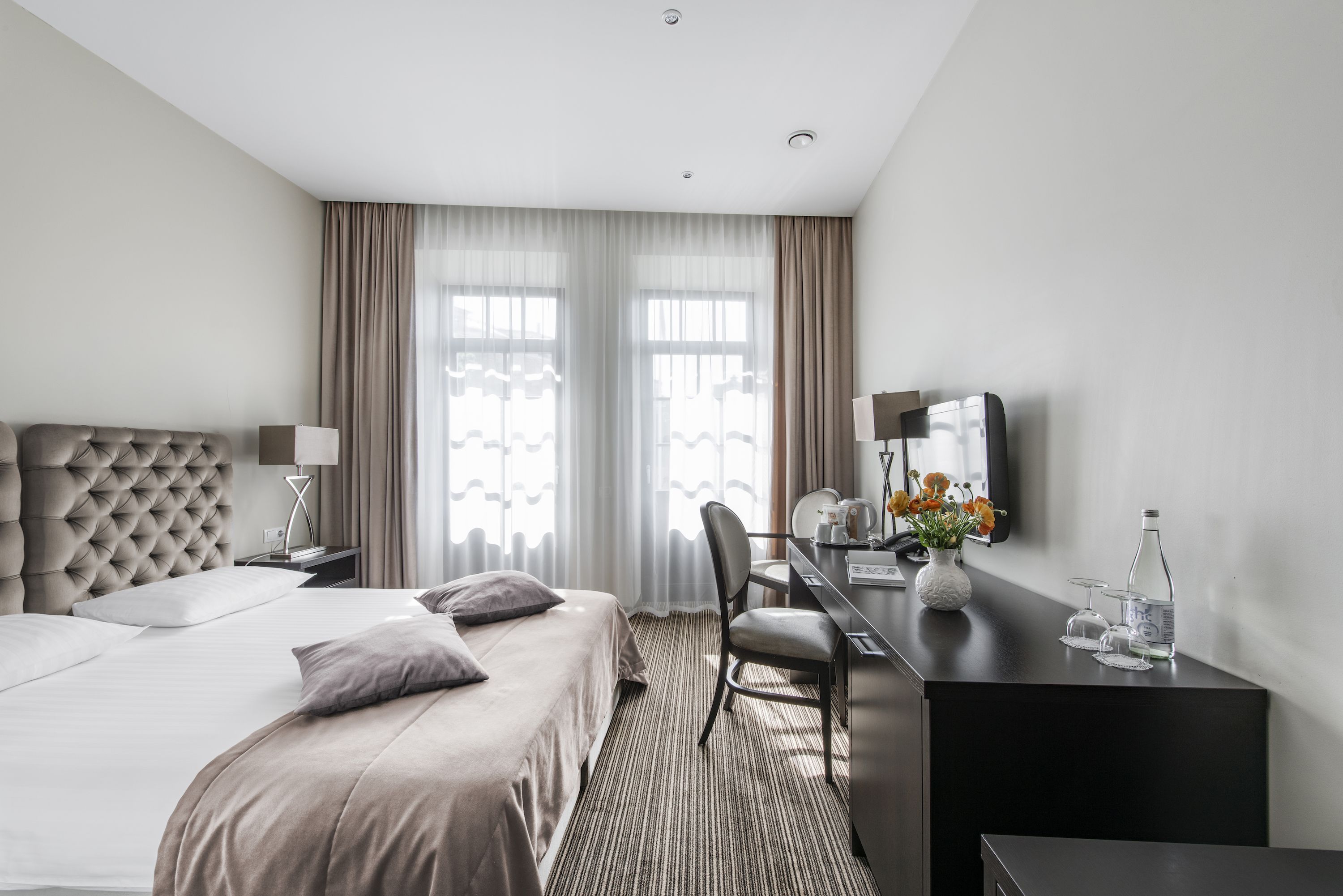 A hotel room with a large bed, a desk with a chair, a television, and a window with curtains.