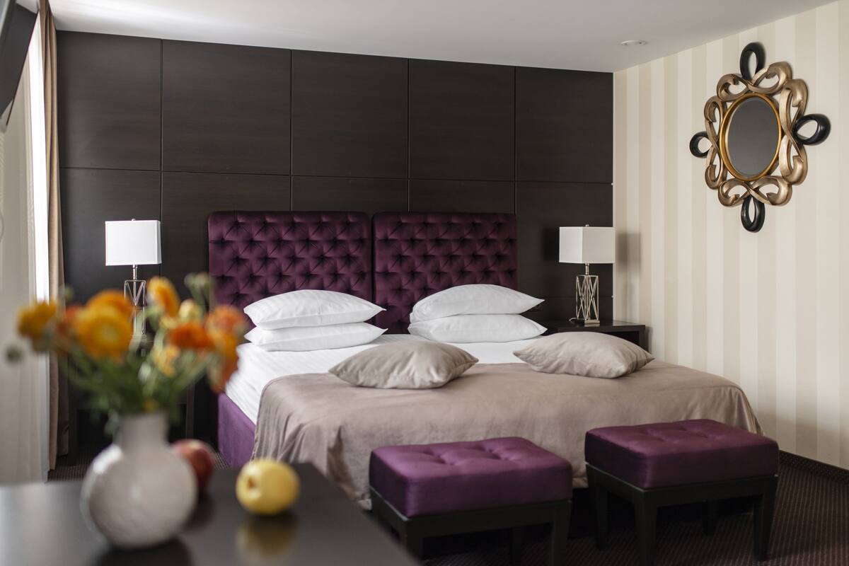 Camera d'albergo con un letto grande, due comodini, un vaso con fiori e una ciotola di frutta.