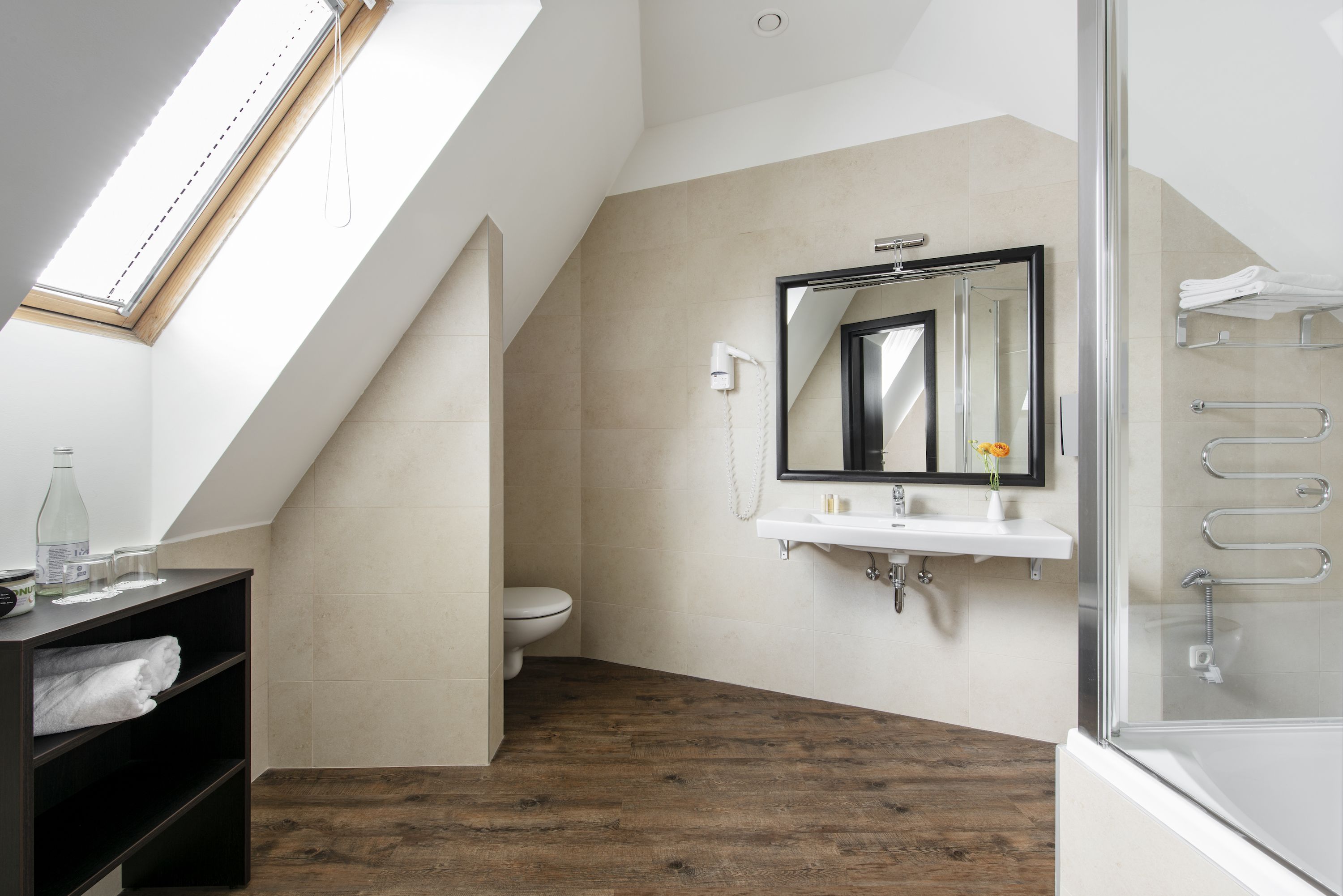 Une salle de bain moderne dotée d’une lucarne, d’une cabine de douche en verre et d’un plancher en bois.