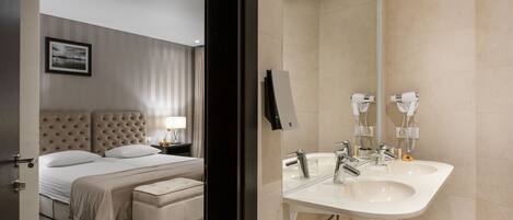 Een moderne hotelkamer met een groot bed, een nachtkastje met een lamp, en een badkamer met een wastafel en spiegel.