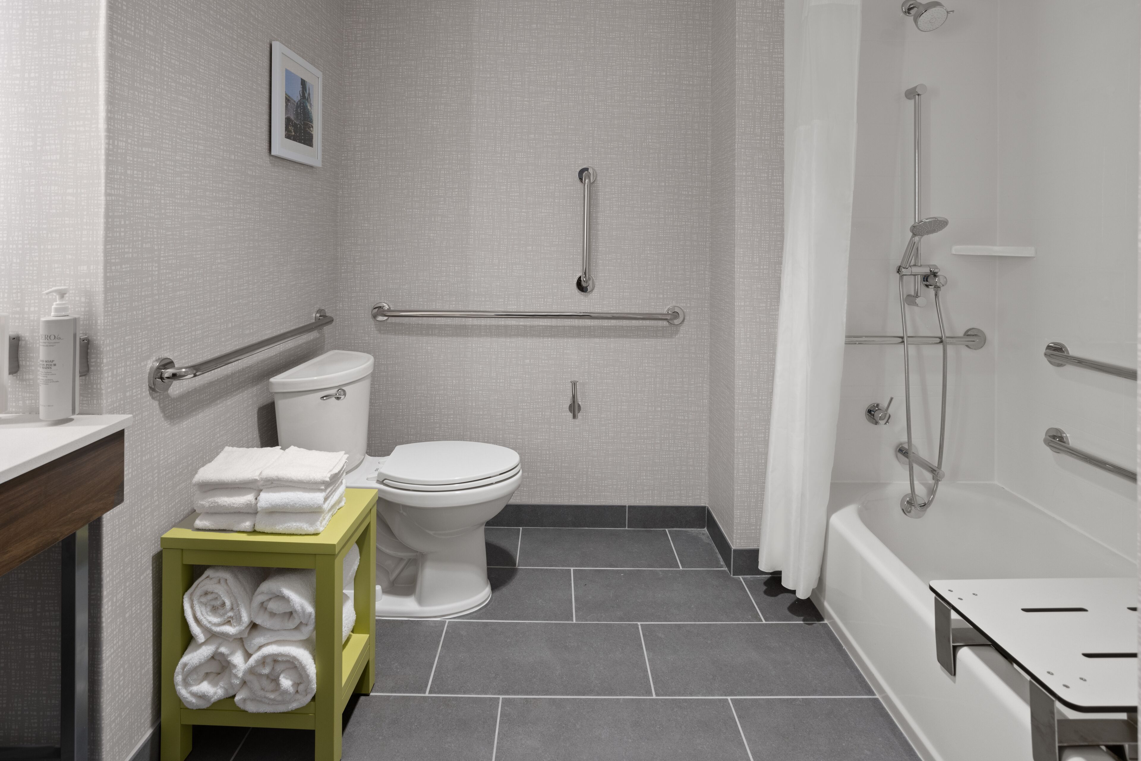 Un baño moderno con inodoro, barras de apoyo, ducha y toallero.