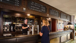 A bar area with a bartender preparing drinks and a customer standing at the counter.