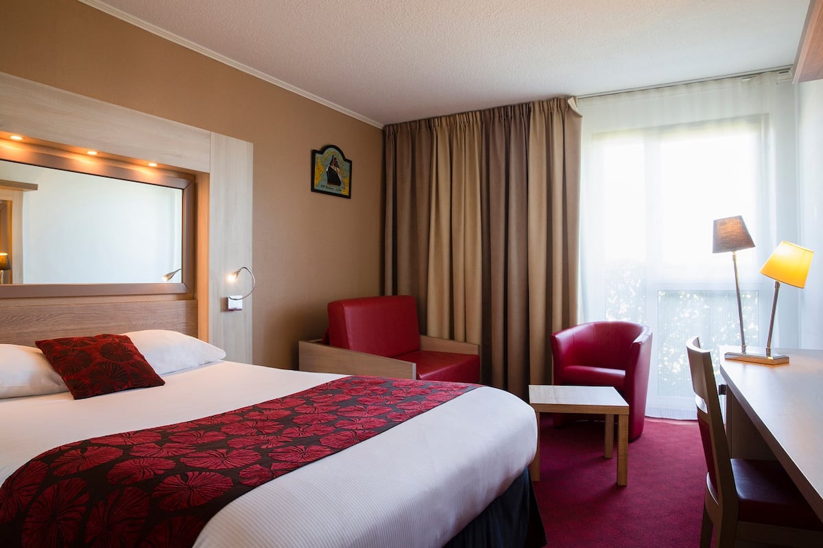 A hotel room with a large bed, a desk, a chair, and a small table.