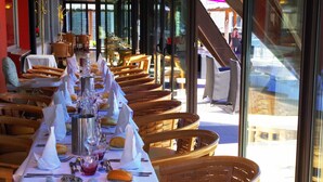A restaurant with a long table set for a meal, wooden chairs, and a view of the outside.