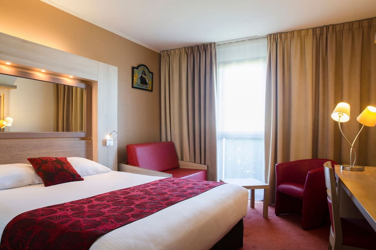 A hotel room with a large bed, a desk, a chair, and a small table.