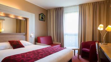 A hotel room with a large bed, a desk, a chair, and a small table.