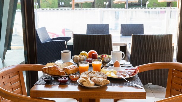 A breakfast table with croissants, fruit, and juice, overlooking a well-manicured garden with umbrellas.