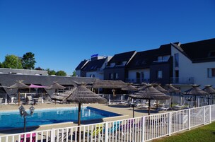 Piscina con sombrillas y sillas de descanso, rodeada por una valla blanca.