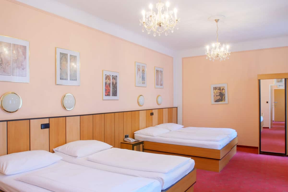 A hotel room with two single beds, a wooden headboard, a chandelier, and framed pictures on the wall.