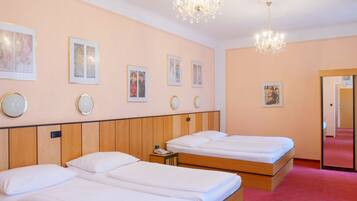 Een hotelkamer met twee eenpersoonsbedden, een houten hoofdbord, een kroonluchter en afbeeldingen in lijsten aan de muur.