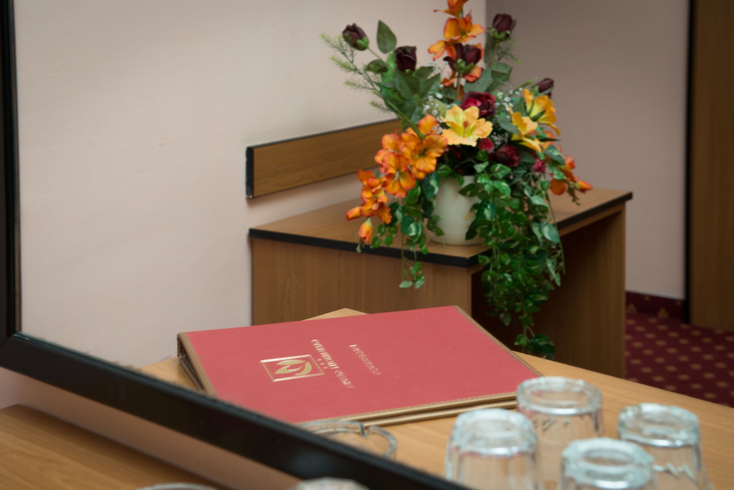 Ein Holztisch mit einem roten Buch, einer Topfpflanze mit Blumen und mehreren klaren Gläsern.
