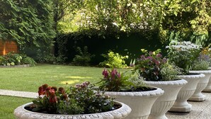 A row of large, white, freestanding planters with various plants and flowers. - Garten - & Kunsthotels Gabriel (Vienna)
