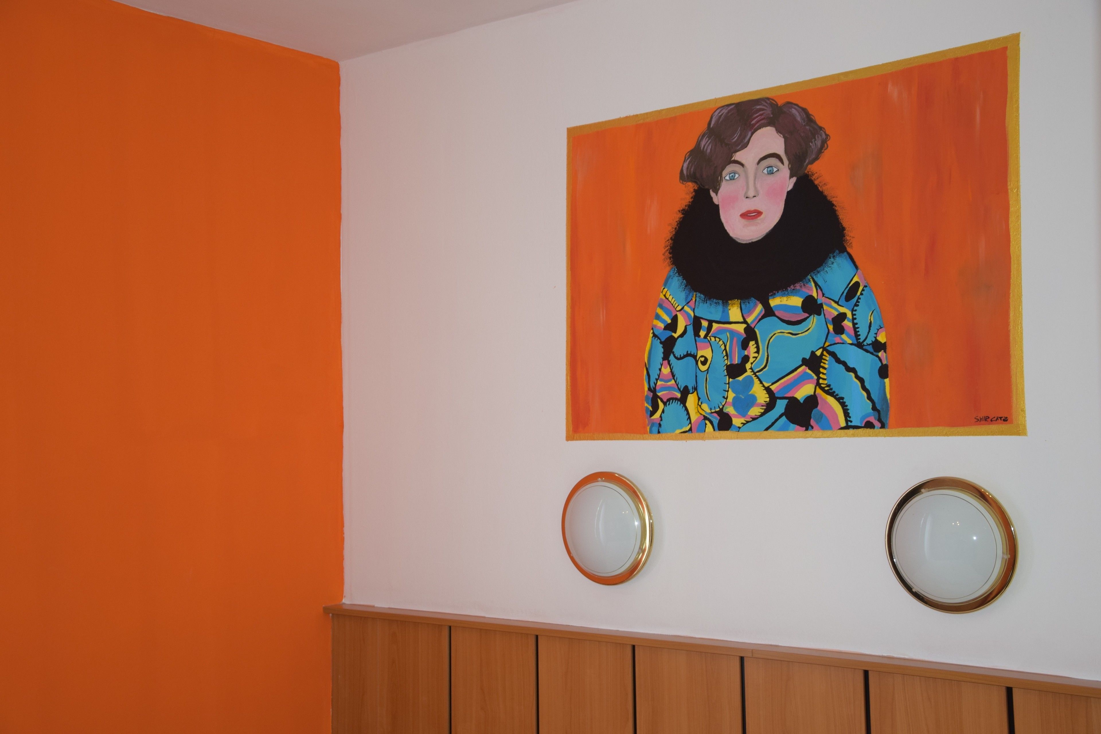A room with an orange wall, a colorful painting, and two round mirrors.