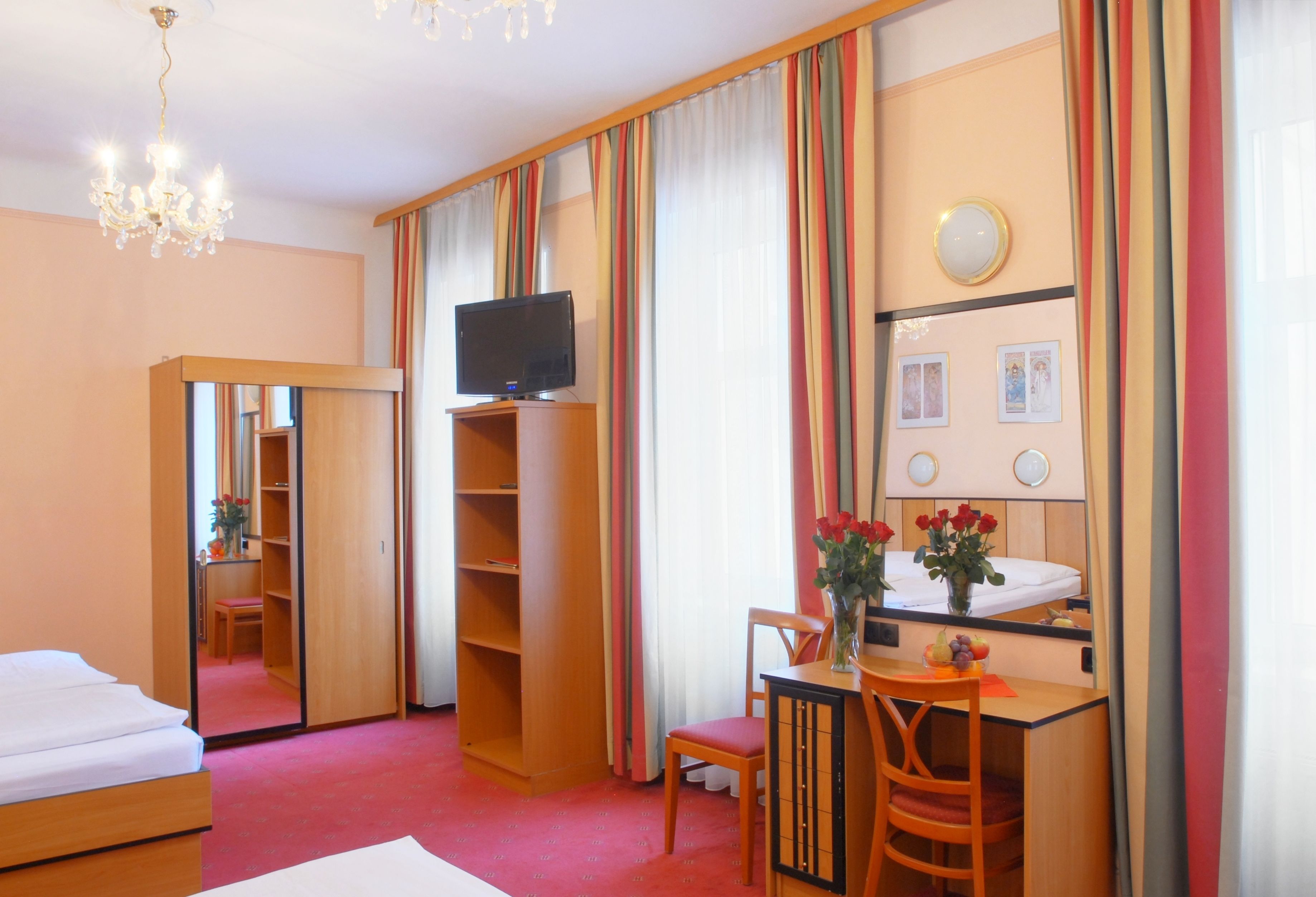 Una habitación de hotel con cama, escritorio con silla, televisor, espejo y armario.