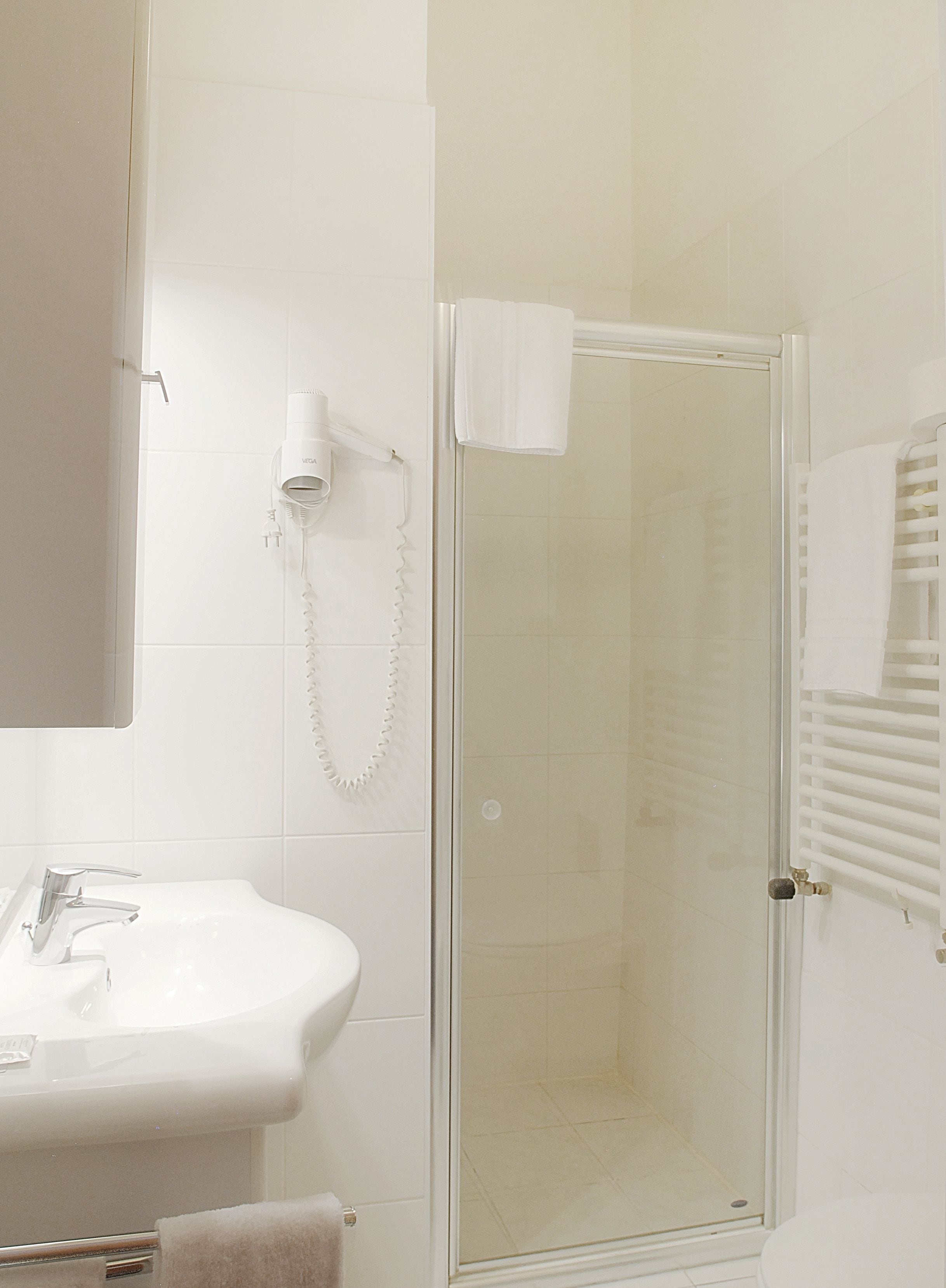 A bathroom with a glass-enclosed shower, a white sink, and a hairdryer mounted on the wall.