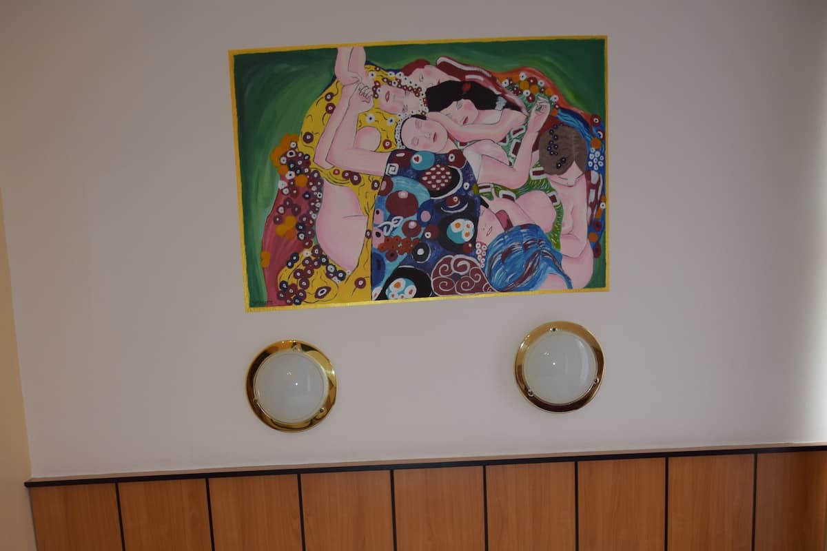 A hotel room with two single beds, a wooden headboard, two bedside tables, and a colorful painting on the wall.
