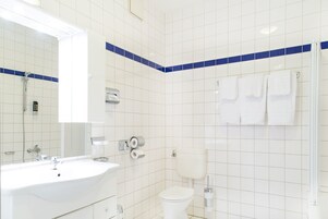 Uma casa de banho com uma sanita, lavatório branco e um espelho. As paredes têm azulejos azuis e há um suporte de toalhas com toalhas.