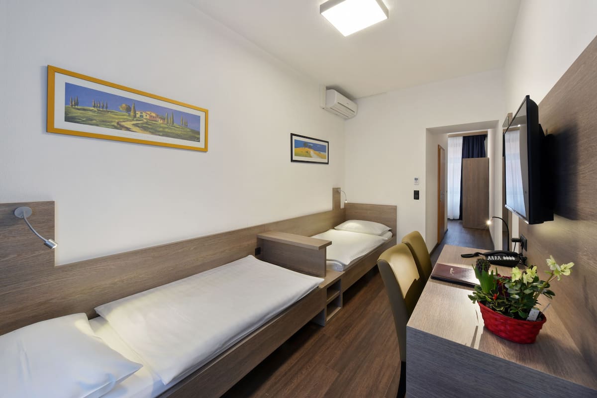Ein Hotelzimmer mit zwei Einzelbetten, einem Schreibtisch mit Stuhl, einem Fernseher und einer Topfpflanze.
