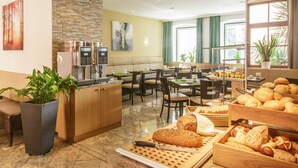 A hotel dining area with a coffee machine, seating, and a variety of breads and pastries. - Lucia Hotel (Vienna)