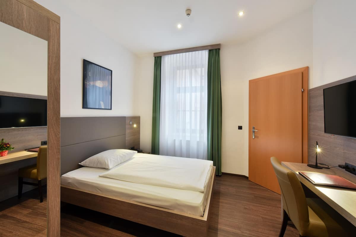 Ein Hotelzimmer mit Bett, Schreibtisch, Stuhl, Fernseher und einer Tür.