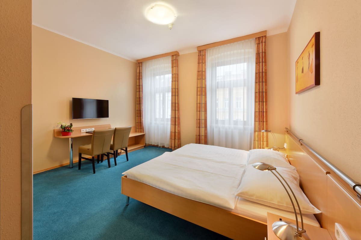 Ein Hotelzimmer mit Bett, Schreibtisch, Stuhl, Fernseher und Vorhängen.