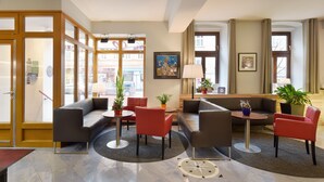 Un hall d’hôtel comprenant un espace salon, un comptoir d’accueil et une grande fenêtre donnant sur la rue.