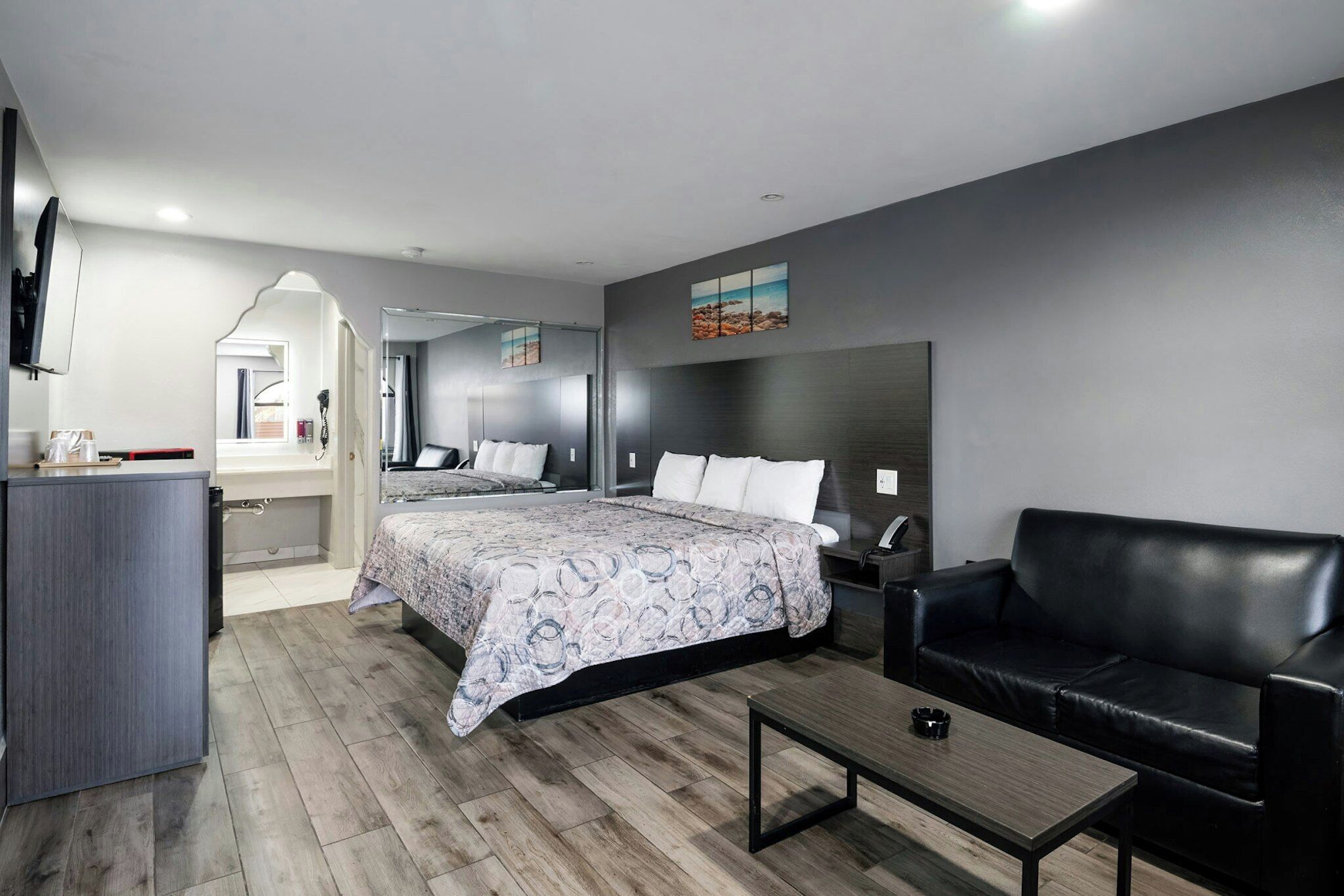 A modern hotel room with a bed, a sofa, a desk, and a TV.