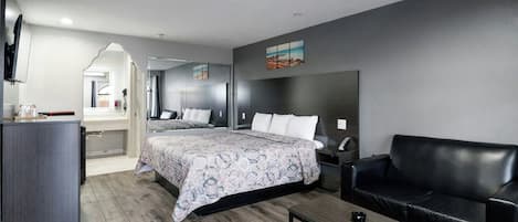 A modern hotel room with a bed, a sofa, a desk, and a TV.