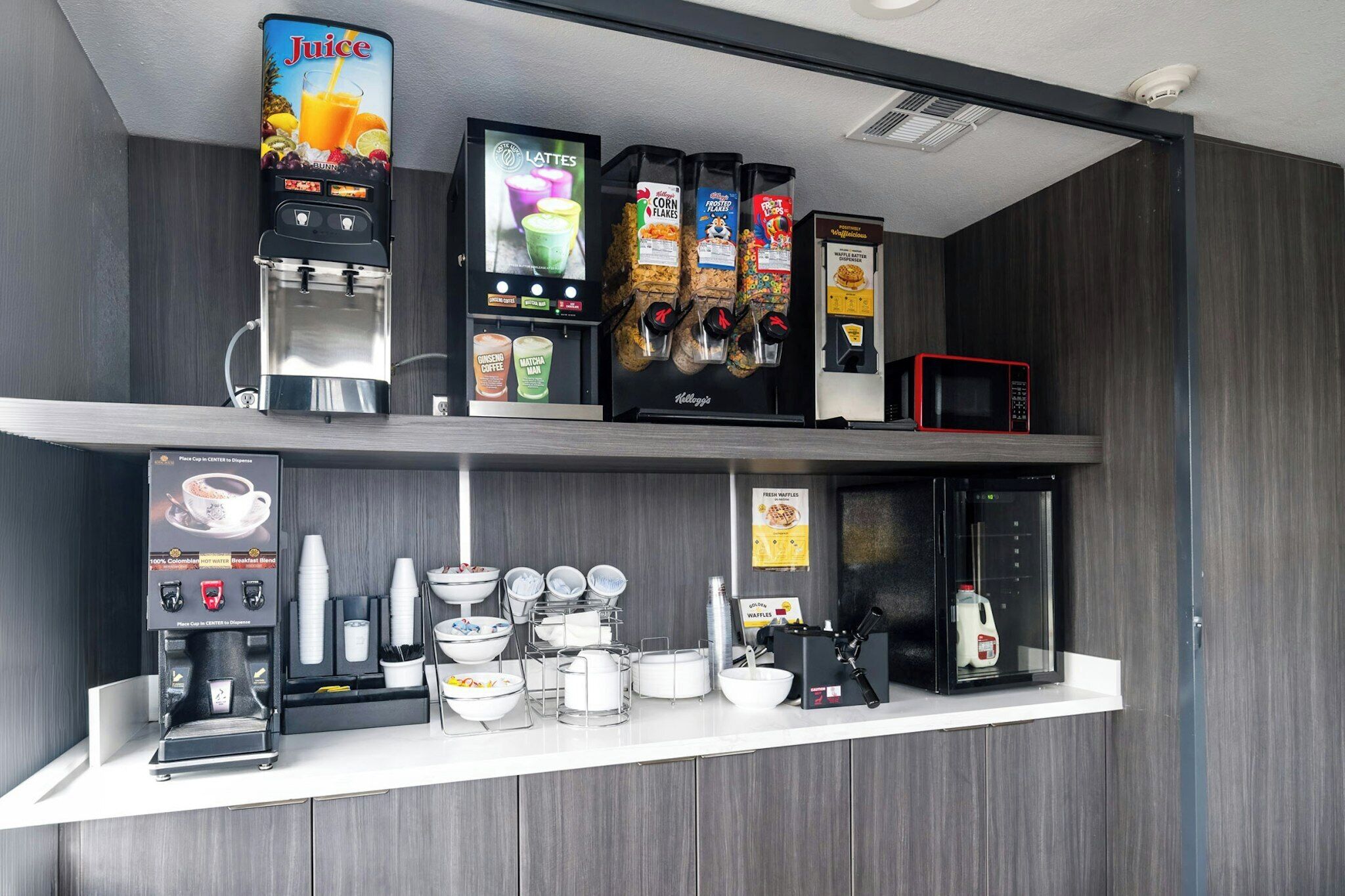 Una estación de bebidas de autoservicio con máquina de café, dispensador de jugo y microondas.