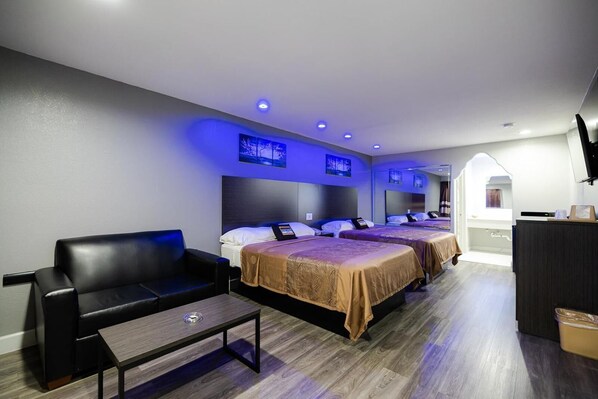 A hotel room with two beds, a sofa, a small table, and a TV. - Downtowner Inns Houston (Houston)