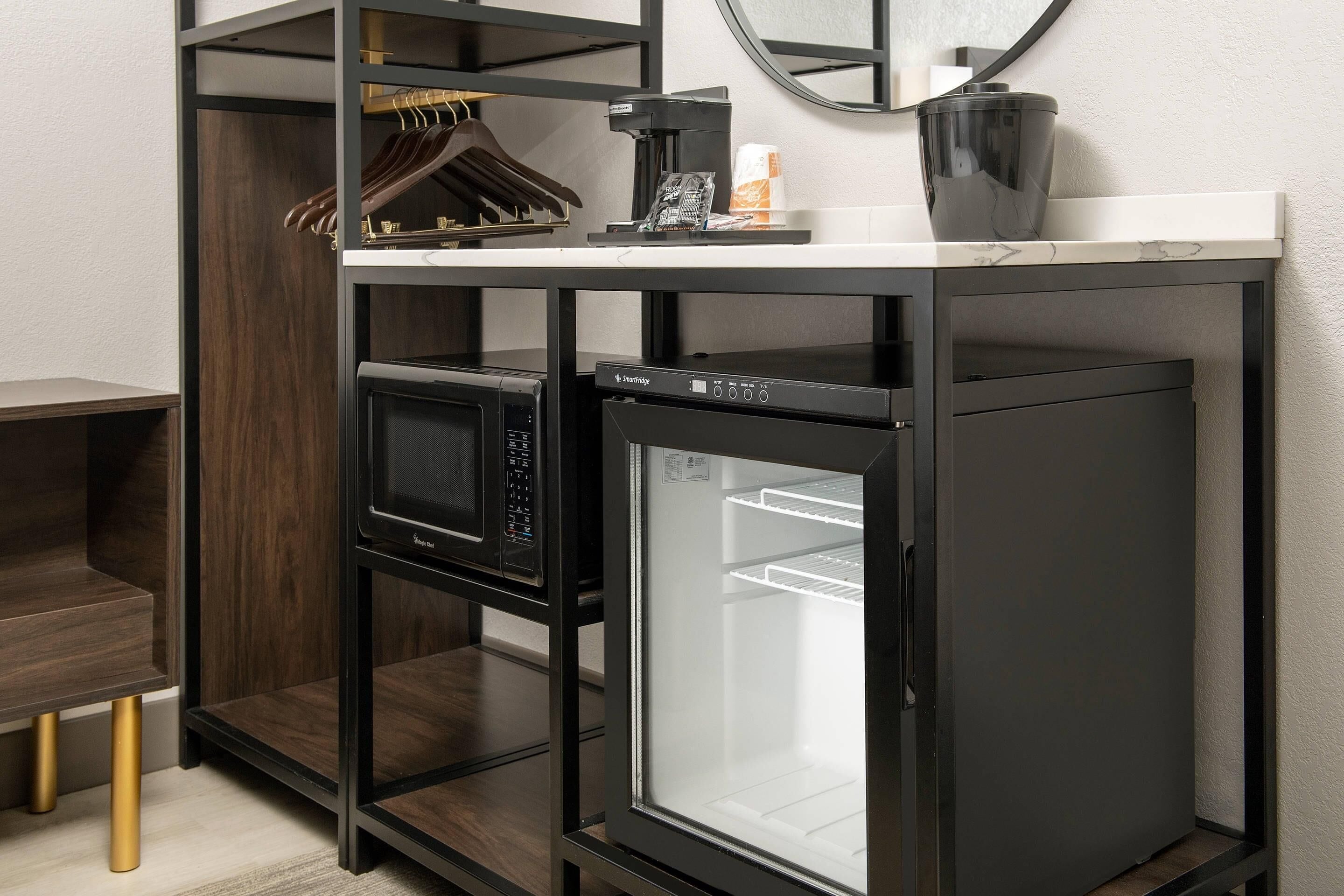 Une petite cuisine équipée comprenant un four à micro-ondes, un réfrigérateur et une machine à café, le tout installé sur un plan de travail blanc.