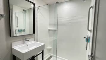 A modern bathroom with a glass-enclosed shower, a white sink, and a large mirror.